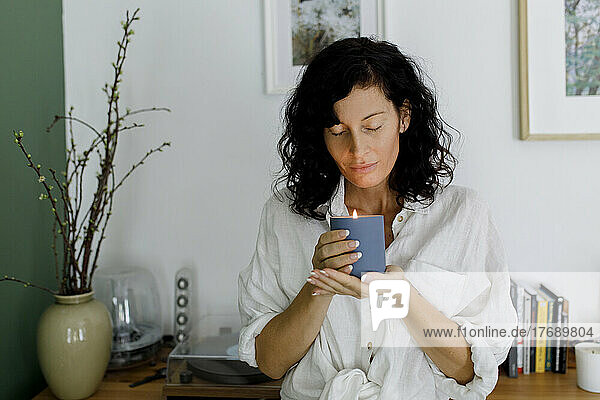 Woman with eyes closed holding candle in living room at home