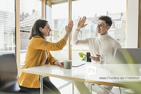Young businessman and businesswoman high fiving in office