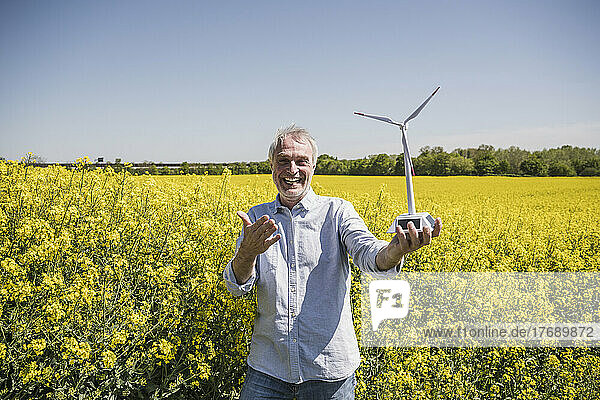 Glücklicher Mann mit Modell einer Windkraftanlage  der an einem sonnigen Tag in der Ablage steht