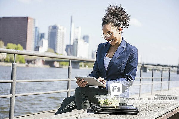Happy businesswoman using tablet PC sitting on bench