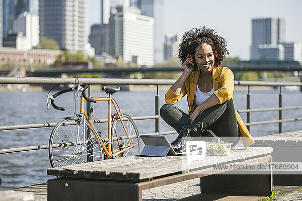 Businesswoman listening music sitting on bench at sunny day