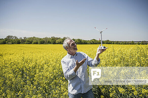 Happy senior man holding model of wind turbine standing in field
