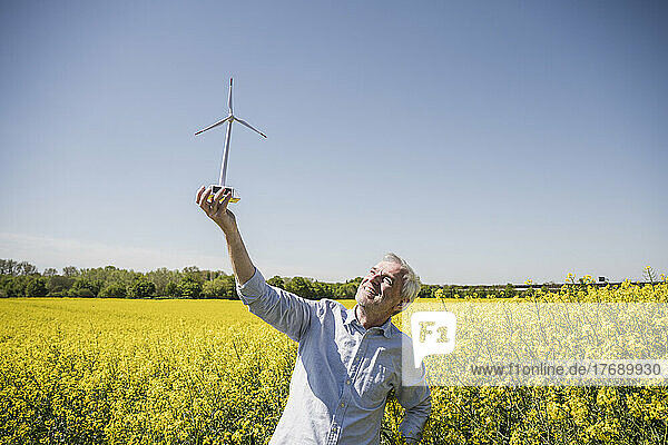 Smiling man looking at model of wind turbine standing in field