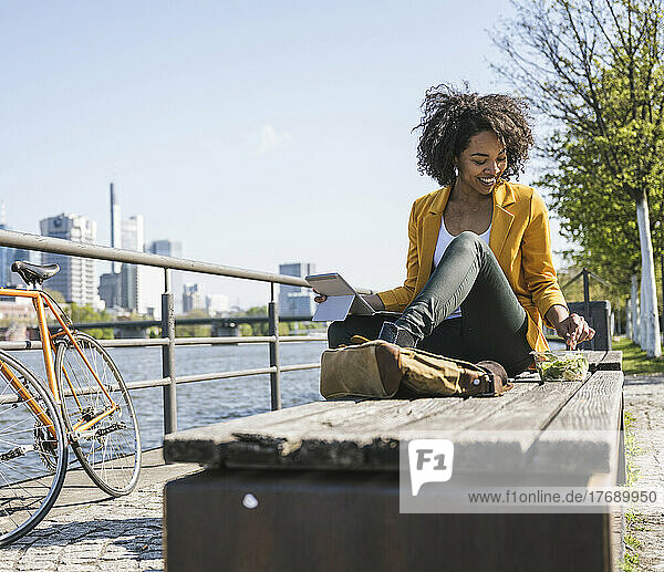 Young businesswoman with laptop having food on bench