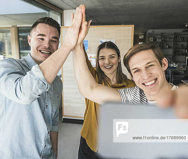 Happy business people high fiving and taking a selfie in office