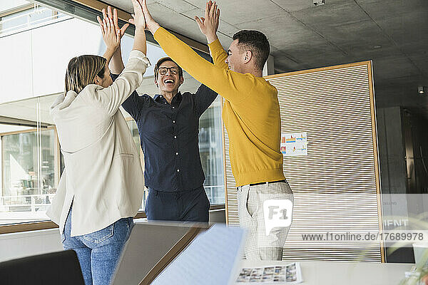 Happy business people standing together with raised arms in office