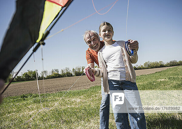 Happy girl and grandfather with kite standing on field