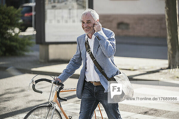 Happy businessman walking with bicycle on sunny day