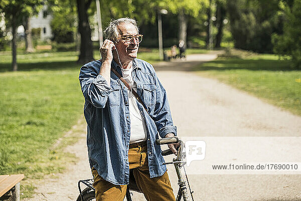 Smiling senior man wearing In-ear headphones with bicycle at park