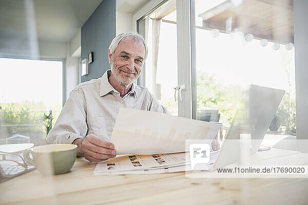 Happy businessman with documents sitting at home