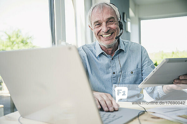 Happy freelancer with tablet PC and laptop sitting at table