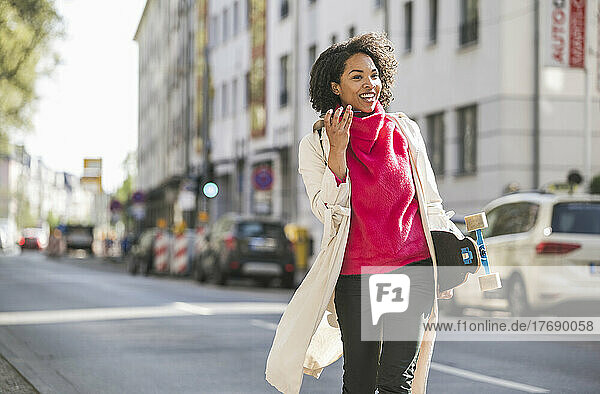 Happy businesswoman using mobile phone walking on street in city