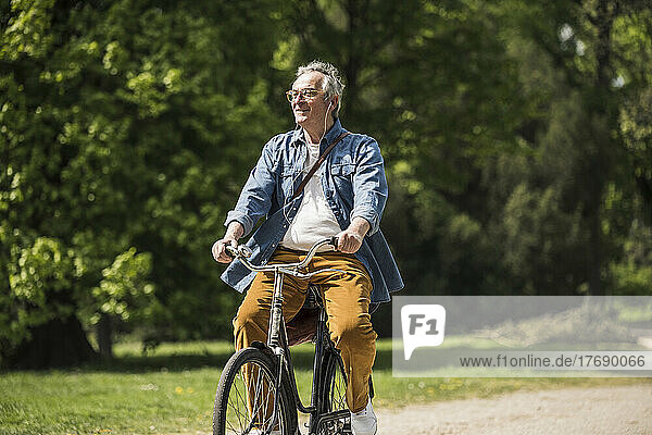 Lächelnder Mann mit Brille  der an einem sonnigen Tag im Park Fahrrad fährt