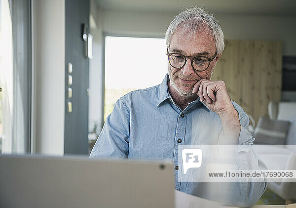 Senior freelancer wearing eyeglasses working on laptop at home