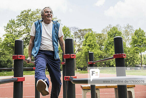 Happy active senior man exercising on gymnastics bar at park