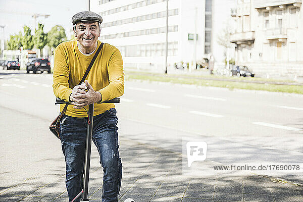 Happy senior man with hands clasped leaning on electric push scooter