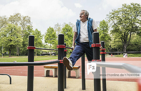 Smiling active senior man exercising on gymnastics bar at park
