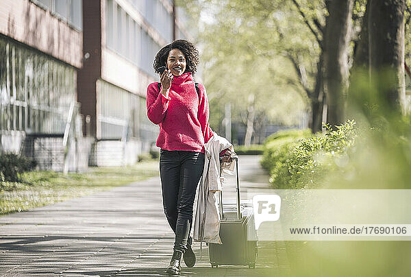 Businesswoman walking with wheeled luggage on footpath