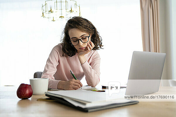 Student schreibt am Laptop am Tisch in ein Buch