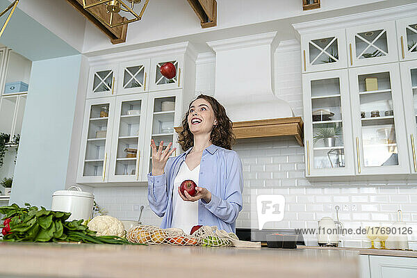 Happy woman juggling with apples in kitchen at home