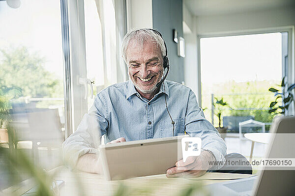 Happy freelancer wearing headset using tablet PC at home