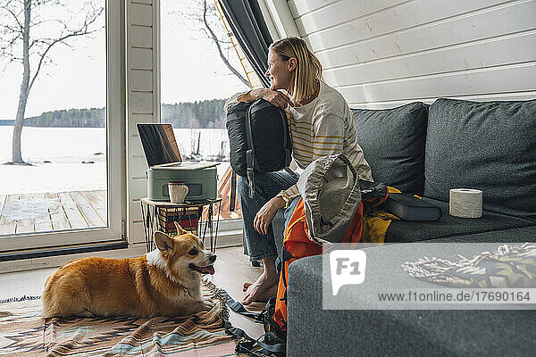 Woman with backpack sitting on sofa by dog at home