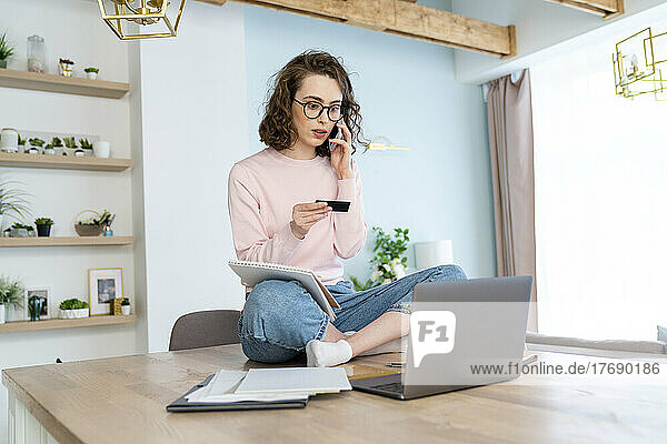 Young woman with credit card doing online shopping through laptop at home