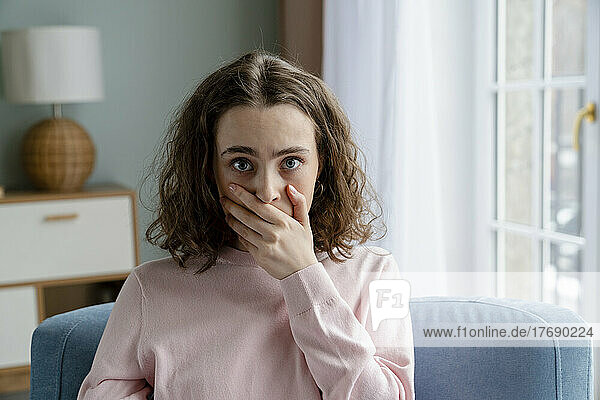 Young woman covering mouth with hand at home