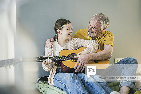 Happy girl with grandfather learning guitar at home