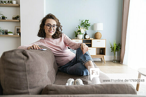 Lächelnde Frau sitzt zu Hause auf dem Sofa
