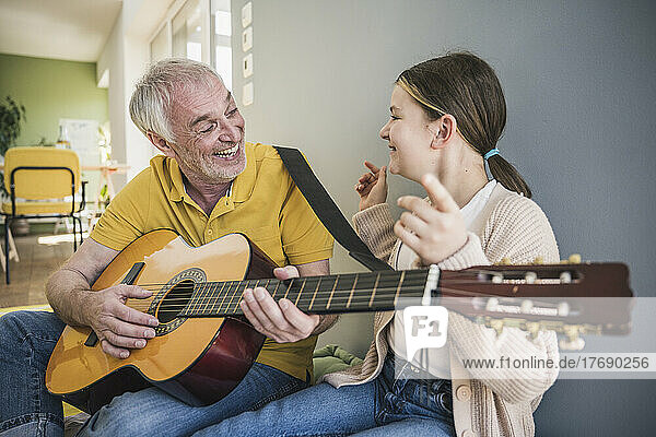 Happy senior man playing guitar by granddaughter at home