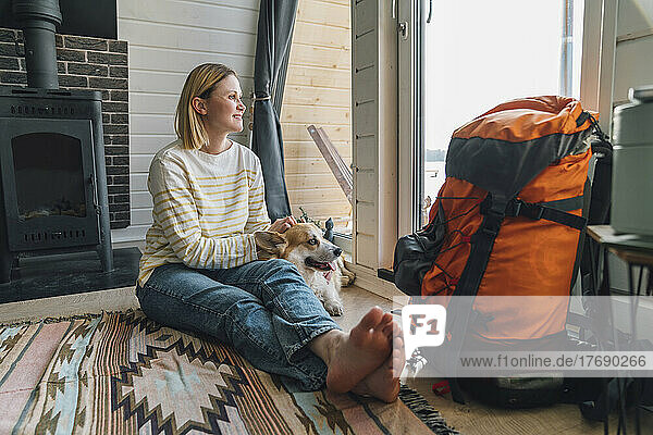 Frau sitzt neben Rucksack und streichelt Hund zu Hause