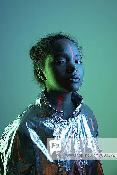 Laser light falling on young woman's face standing against green background