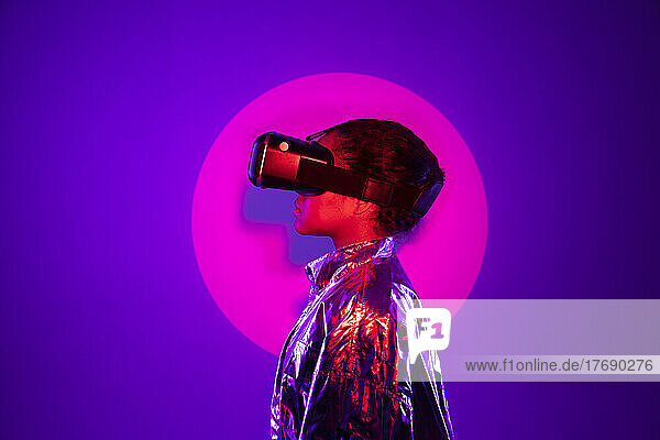 Im Rampenlicht steht eine junge Frau mit Virtual-Reality-Simulator vor violettem Hintergrund
