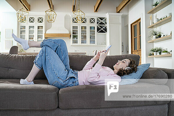 Woman using smart phone lying on sofa