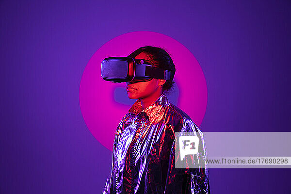 Im Rampenlicht steht eine Frau mit Virtual-Reality-Simulator vor violettem Hintergrund