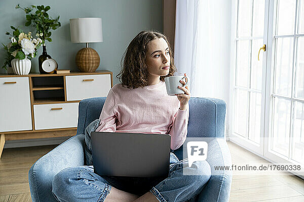 Contemplative businesswoman with laptop and coffee cup in living room