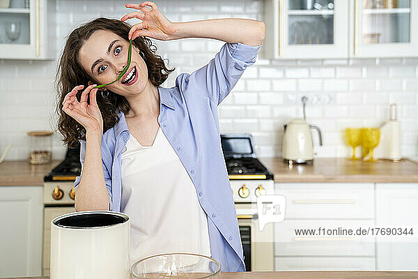 Fröhliche Frau macht zu Hause in der Küche Schnurrbart mit Frühlingszwiebelblatt