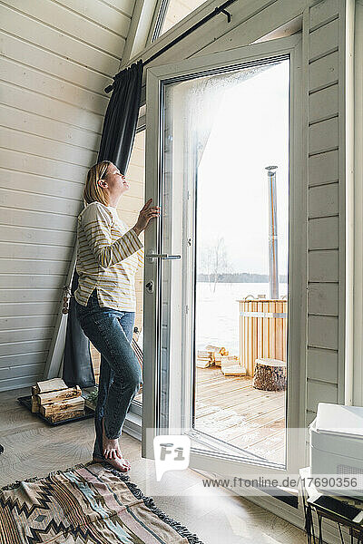 Frau atmet frische Luft ein und öffnet Glastür zu Hause