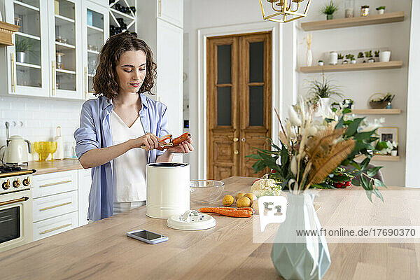 Young woman peeling carrot at dining table in kitchen