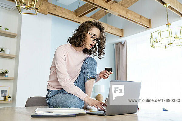 Woman doing online shopping with credit card through laptop at home