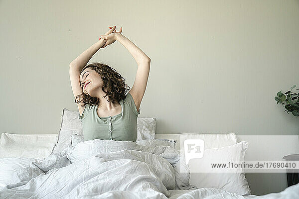 Smiling beautiful young woman stretching on bed at home