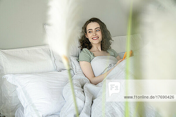 Happy woman with smart phone sitting on bed at home