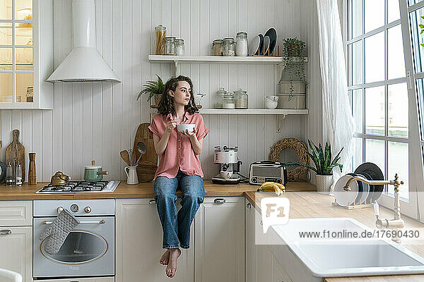 Woman with bowl sitting on kitchen counter at home