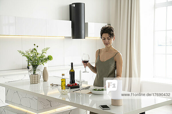 Frau hält Weinglas in der Hand und bereitet zu Hause in der Küche eine Mahlzeit zu