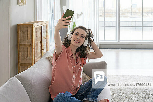 Lächelnde junge Frau  die zu Hause ein Selfie mit dem Smartphone macht