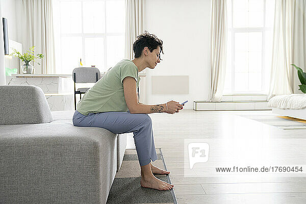 Woman using mobile phone sitting on sofa at home