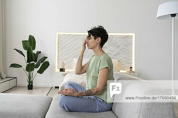 Woman meditating sitting on sofa at home