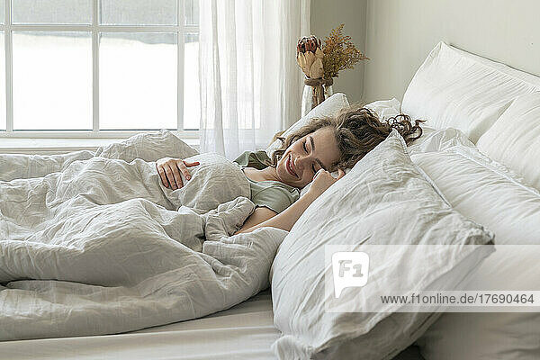 Smiling young woman sleeping in bed at home