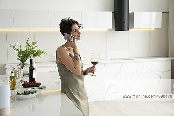 Frau hält Weinglas in der Hand und telefoniert in der Küche